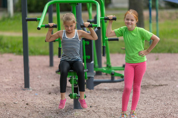 Two little cute girls is engaged in fitness equipment outdoor.