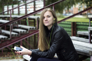 Young beautiful girl look and listening music on your mobile phone  the old stadiums bench