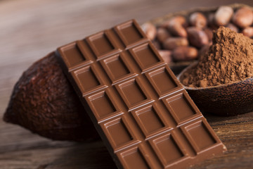 Chocolate bar, candy sweet, cacao beans and powder on wooden bac