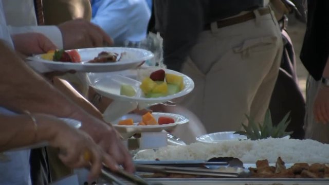 A line of people gather to get food on chaffing dishes at a catered Hawaiian party. HD 1080.
