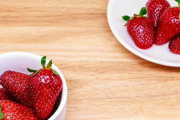 Fresh strawberry in cup and dish on wooden background