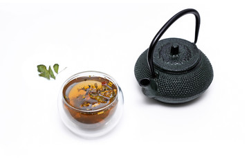 Iron asian-styled teapot and glass cup with herbal tea - dried herbs, leaves and flowers.  Isolated on white background.