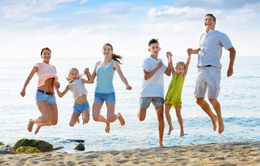 Large family jumping up together on beach on clear summer day