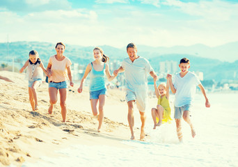 Family with four kids happily running on beach