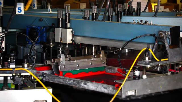 A pneumatic silk screening printing press operates.