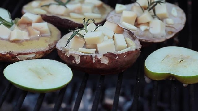 Cooking porcini mushrooms filled with scamorza cheese and green apples in slices on hot barbecue grill.