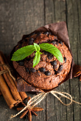 chocolate dark muffin with a leaf of mint on a wooden table with cinnamon, anise, chocolate