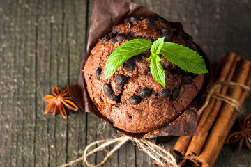 chocolate dark muffin with a leaf of mint on a wooden table with cinnamon, anise, chocolate