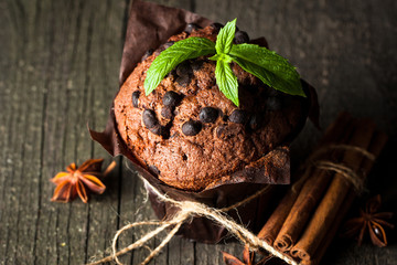 chocolate dark muffin with a leaf of mint on a wooden table with cinnamon, anise, chocolate