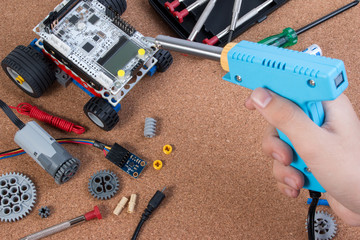 Hand holding soldering iron tool assembling robot with microcontroller.