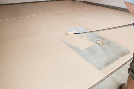 Worker Painting Floor of Garage with Roller.