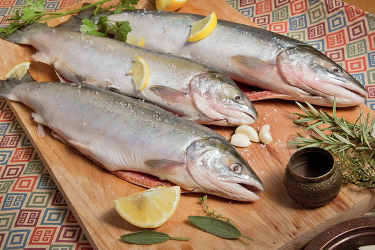  Three raw seabass with spices on an old wooden background.