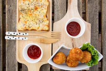 Rectangular  pizza with topping and cheese balls on a wooden table,pizza and cheese balls with knife and spoon ,pizza and cheese balls with sauce.