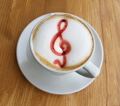 Delicious cappuccino cup with froth and musical G clef sign out of sugary cream