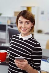 frau im büro mit handy und einer tasse tee