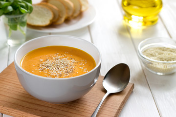 Healthy pumpkin soup with sesame in gray bowl on a white table.