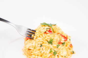 Risotto with chicken, tomatoes, bell pepper, onion and garlic on a white plate decorated with parsley being eaten with a fork