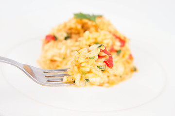 Risotto with chicken, tomatoes, bell pepper, onion and garlic on a white plate decorated with parsley being eaten with a fork