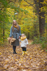 Mother and little daughter blonde walking and playing in autumn park, yellow lives around