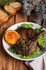 Confit duck legs with thyme and slice of orange in white plate on wooden background.  New year food. Selective focus