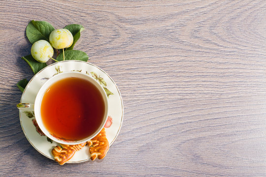 Чашка чая, печенье, желтая слива на деревянном фоне