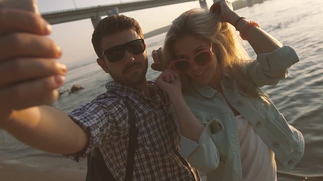 Young happy couple taking photo with cell phone outside at the beach