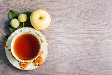 Чашка чая, печенье, желтая слива и яблоко на деревянном фоне