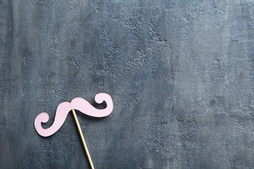 Paper mustache on a stick on grey wooden table