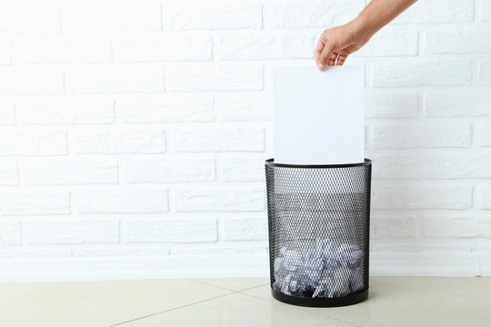 Male hand throwing blank sheet of paper into metal trashcan
