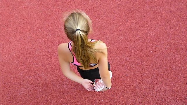 Top view of teenager girl athlete stretching before running on a stadium, slow motion