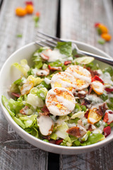 Fresh organic Cobb salad topped with homemade Ranch dressing, hard boiled eggs, bacon, peppers, peas, and green onions on an old weathered barn wood table
