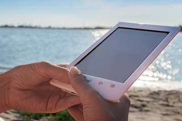 wooman sitting on sandy beach and holding bookreader