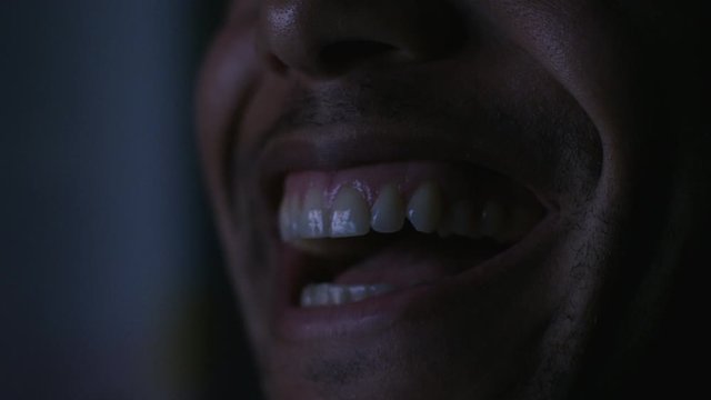 Close up on male mouth as they laugh whilst watching something at night in the dark