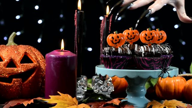Halloween party table with spooky hand with long black nails hovering over chocolate cupcakes.