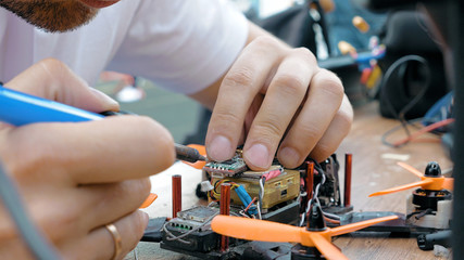 Close up of man's hands welding details while assembling FPV drone using tools, preparing quadcopter for flight. Repair drone before training process.