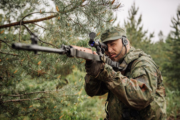 army soldier holding sniper rifle with scope and aiming in forest. war, army, technology and people concept


