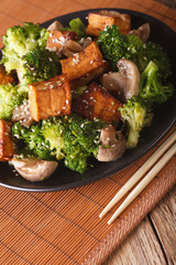 Fried tofu with broccoli, mushrooms and sesame close-up in asian style. vertical
