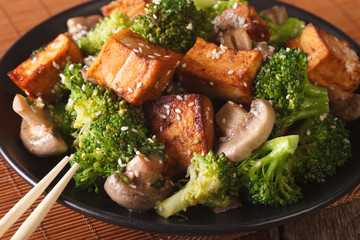 Vegetarian food: fried tofu with broccoli, mushrooms and sesame close-up. horizontal
