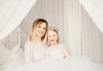 Mother and daughter like brides in white dress on the bed.