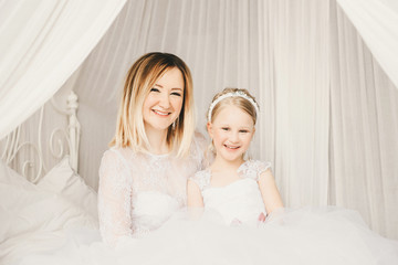 Mother and daughter like brides in white dress on the bed.