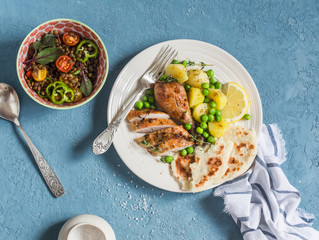 Lemon thyme baked chicken, boiled potatoes with green peas, salad with lentils and tomatoes on a blue background. Top view