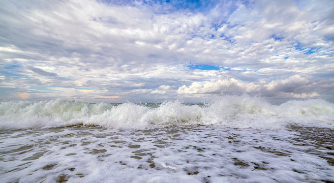 Fototapeta White waves of Black Sea with reflections of curly sunset clouds