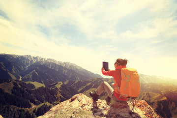 successful woman backpacker use digital tablet taking photo on mountain peak cliff