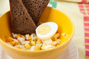 Salad with eggs and carrot in a yellow cup with black bread