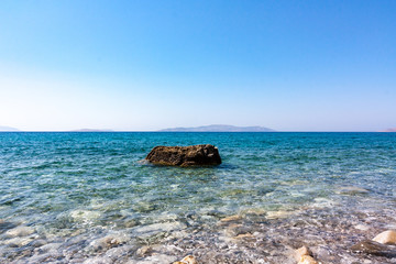 Single rock in clear sea water with blue sky