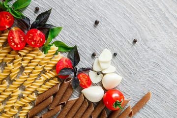 Mixed of two colored pasta near tomatoes, garlic and basil on grey wooden  background. Raw  frame. Copy space.
