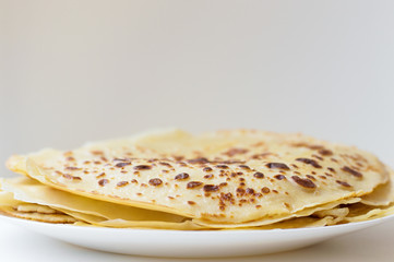 Thin homemade pancakes on white plate. Pile of fresh crepes. Horizontal photo of fried crepes with crispy edges on grey and white background