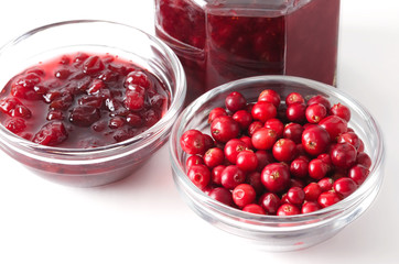 Lingonberries and lingonberry jam in glass bowls over white. Fresh red fruits of Vaccinium vitis-idaea, also mountain cranberries, partridgeberries or cowberries. Staple food in Scandinavian cuisine.