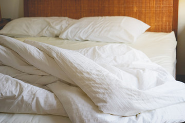 Fototapeta na wymiar Messy white bedding sheets in selective focus on bed with morning light
