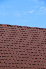 Modern roof covered with tile effect PVC coated brown metal roof sheets against a blue sky